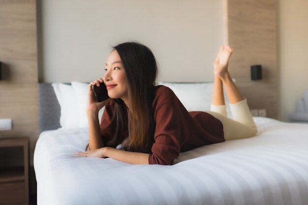 Schöne junge asiatische Frauen des Porträts, die Handy auf Bett verwenden