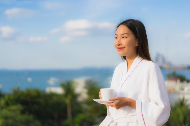 Schöne junge asiatische Frauen des Porträts halten Kaffeetasse in der Hand um Ansicht im Freien