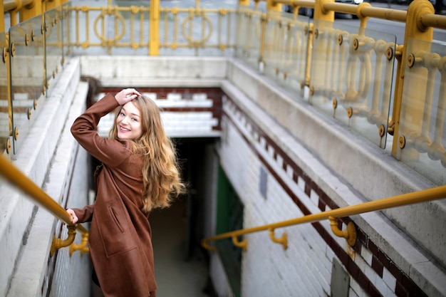 Schöne junge blonde Frau, die lächelt, während sie auf der Treppe posiert, die zum Untergrund führt