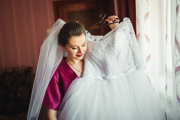 Schöne junge Braut mit Hochzeitsmake-up und -frisur im Schlafzimmer