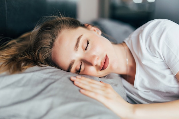 Schöne junge brünette Frau, die in einem weißen Bett schläft