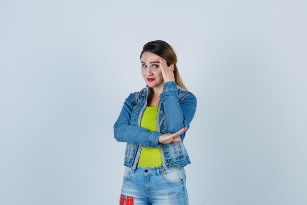 Schöne junge Dame, die das Gesicht hinter der Hand in Denim-Outfit versteckt und beschämt aussieht, Vorderansicht.