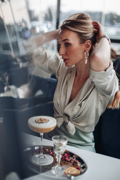 Schöne junge Dame, die ihr blondes Haar hält und einen Pferdeschwanz vor dem Frühstück im Café macht