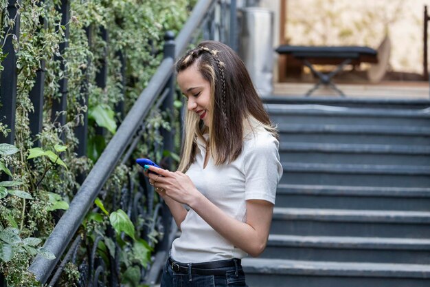 Schöne junge Dame lächelt und spielt mit ihrem Telefon auf der Straße