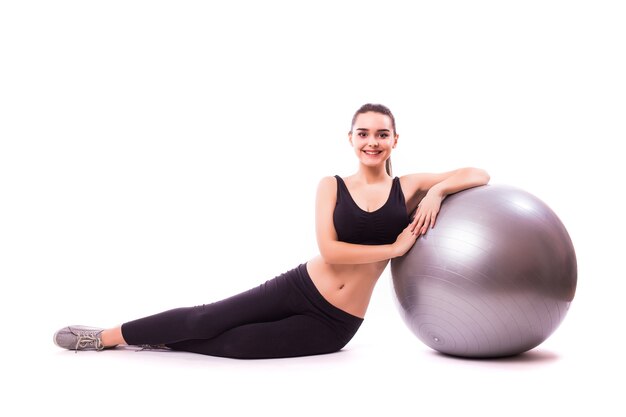 Schöne junge Fitnessfrau mit Gymnastikball, die auf weißem Hintergrund lokalisiert