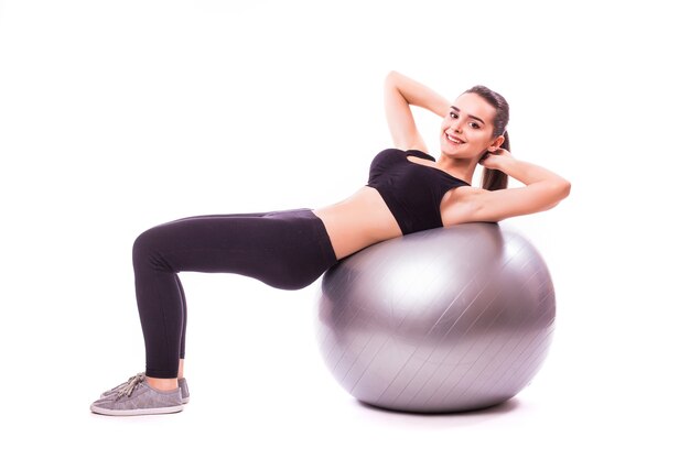 Schöne junge Fitnessfrau mit Gymnastikball, die auf weißem Hintergrund lokalisiert