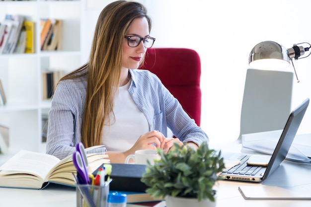 Schöne junge Frau arbeitet mit Laptop in ihrem Büro.