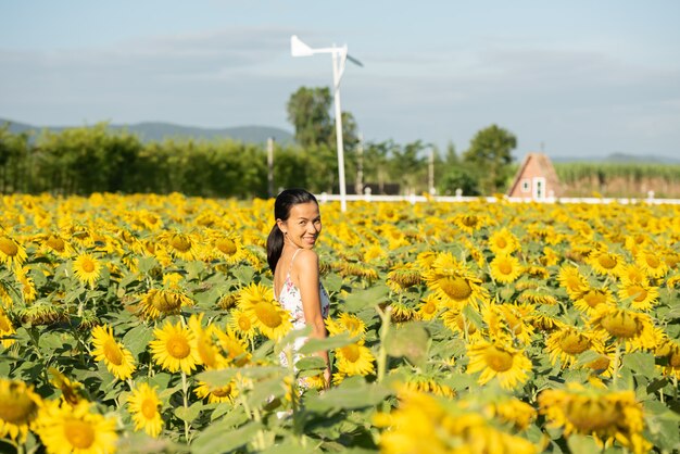 Schöne junge Frau auf einem Sonnenblumenfeld in einem weißen Kleid. Reisen Sie am Wochenende Konzept. Porträt der authentischen Frau im Strohhut. Draußen auf dem Sonnenblumenfeld.