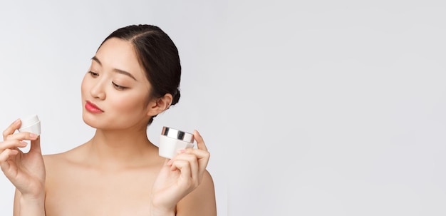 Schöne junge Frau auf weißem isoliertem Hintergrund mit kosmetischer Gesichtscreme asiatisch