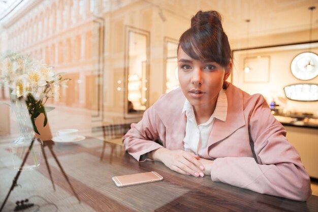 Schöne junge Frau, die am Kaffeetisch sitzt