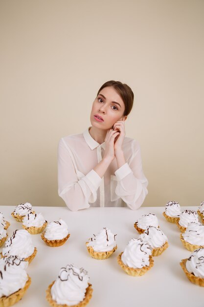 Schöne junge Frau, die am Tisch mit Cupcakes sitzt