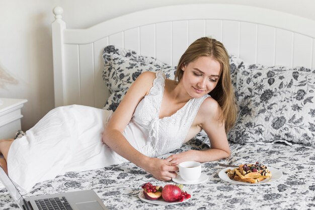 Schöne junge Frau, die auf dem Bett betrachtet Frühstück liegt