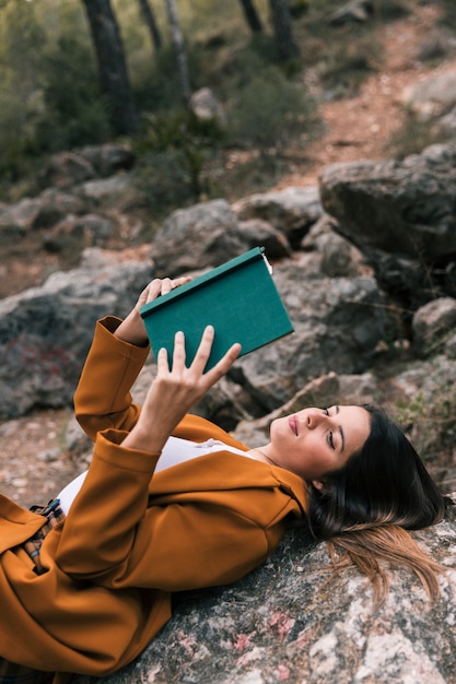 Schöne junge Frau, die auf dem Felsen liest das Buch liegt