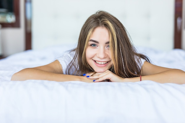 Schöne junge Frau, die beim Liegen auf dem Bett zu Hause in die Kamera schaut