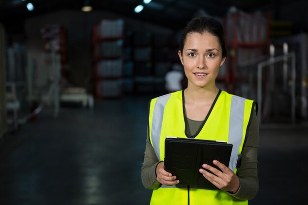 Schöne junge Frau, die digitales Tablett in der Fabrik verwendet