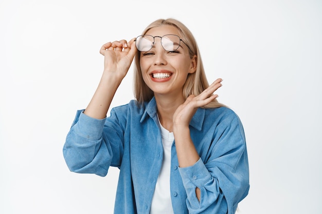 Schöne junge Frau, die eine Brille abnimmt, lächelt und sieht aufgeregt aus, steht glücklich vor weißem Hintergrund Kopieren Sie Platz