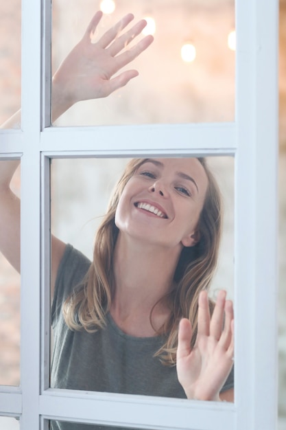 Kostenloses Foto schöne junge frau, die hinter dem fenster aufwirft