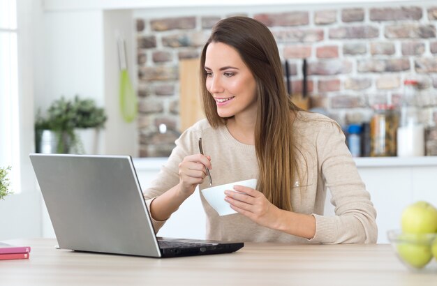 Schöne junge Frau, die ihren Laptop in der Küche verwendet.