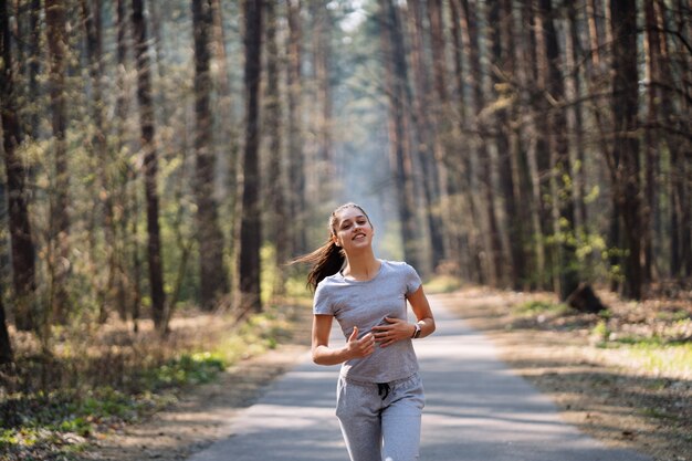 Schöne junge Frau, die im grünen Park am sonnigen Sommertag läuft