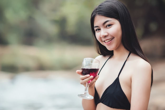 Schöne junge Frau, die im im Freien trinkendes Cocktail sitzt und den Fluss aufpasst