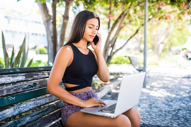 Schöne junge Frau, die im Park mit Laptop und Handy ruht