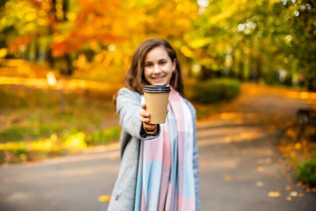 Schöne junge Frau, die Imbisskaffee im Park im Herbst trinkt.