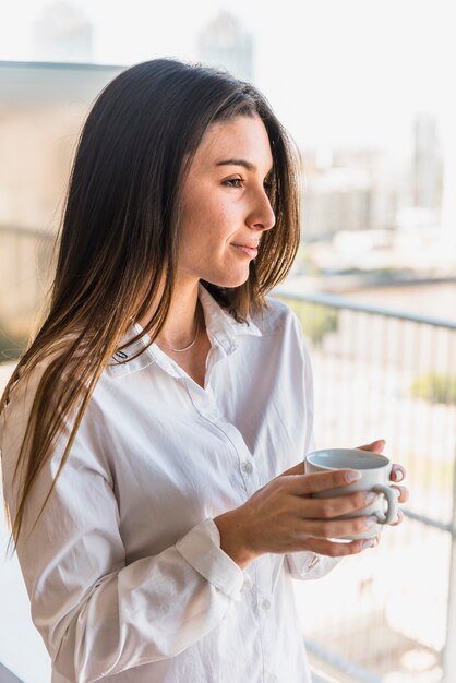 Schöne junge Frau, die in der Hand Kaffeetasse hält