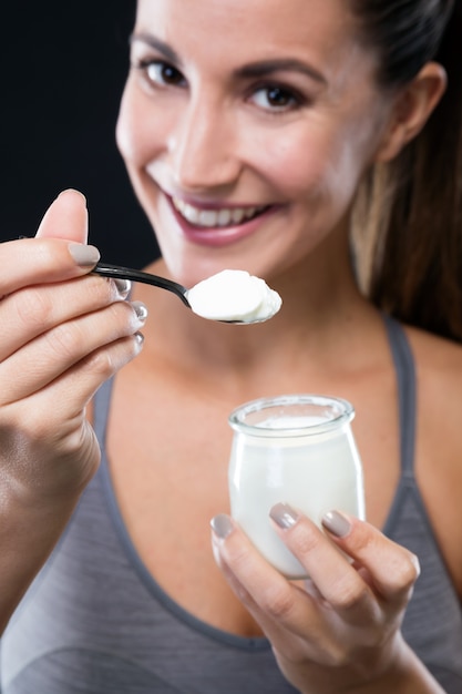 Schöne junge Frau, die Joghurt über schwarzem Hintergrund isst.