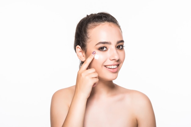 Schöne junge frau, die kosmetik unter den augen lokalisiert auf weißer wand anwendet