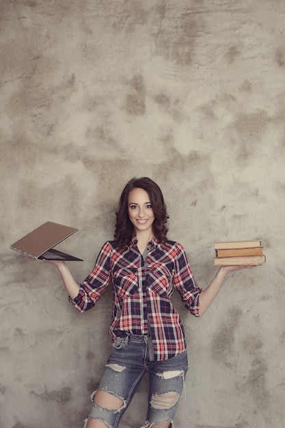 Schöne junge Frau, die mit Büchern und Laptop aufwirft