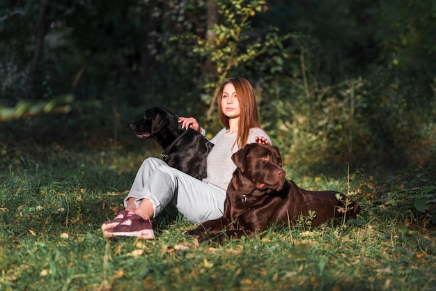 Schöne junge Frau, die mit ihren Haustieren im Park sitzt