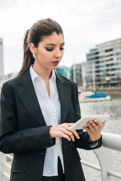 Schöne junge Frau, die nahe dem Hafen sich berührt am Handy steht