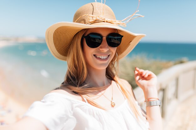 Schöne junge Frau, die selfie am Strand auf Ozean tut