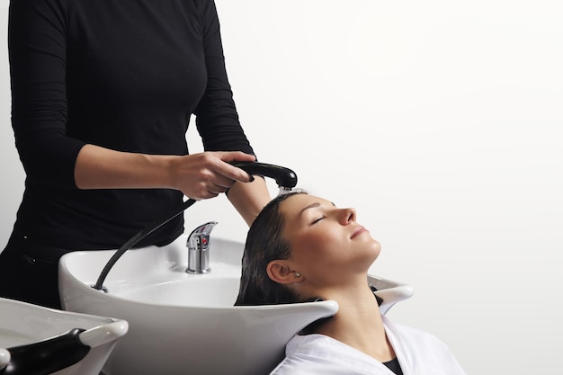 Schöne junge Frau, die sich vom Friseur im Salon die Haare waschen lässt