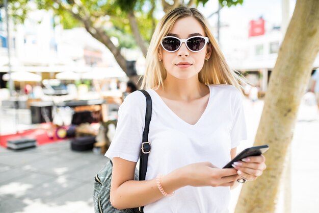 Schöne junge Frau, die Smartphone im Freien in der sonnigen Sommerstraße verwendet