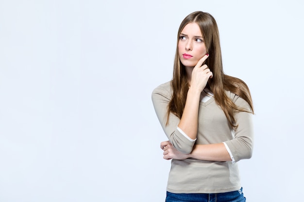 Schöne junge frau, die über weißem hintergrund denkt.