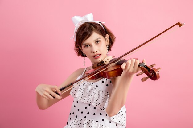 Schöne junge Frau, die Violine über Rosa spielt