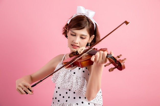 Schöne junge Frau, die Violine über Rosa spielt