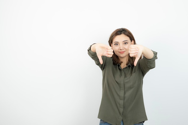 Schöne junge Frau im lässigen Outfit, die steht und Daumen nach unten gibt. Foto in hoher Qualität