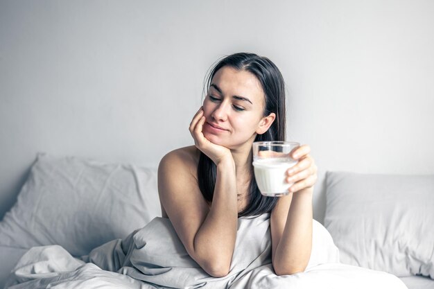 Schöne junge Frau im weißen Bett mit Glas Milch