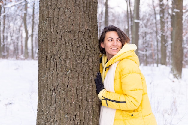 Schöne junge Frau im Winterwald zeigt zarte Gefühle für die Natur, zeigt ihre Liebe zum Baum