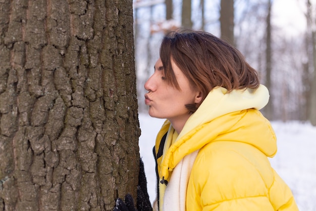 Schöne junge frau im winterwald zeigt zarte gefühle für die natur, zeigt ihre liebe zum baum