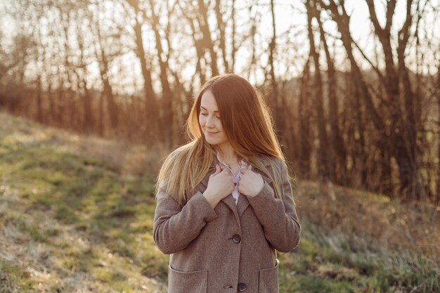 Schöne junge Frau im Wollmantel auf dem Wald bei Sonnenuntergang