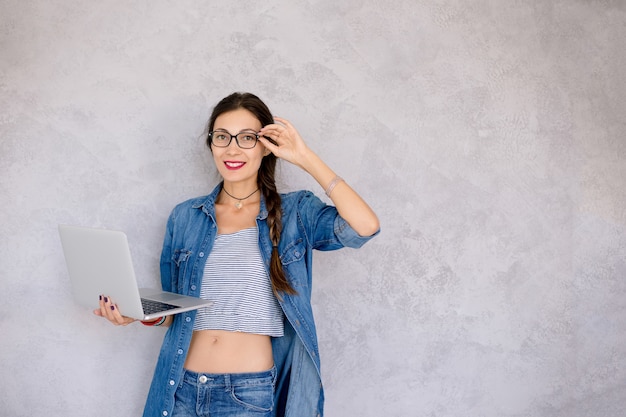 Kostenloses Foto schöne junge frau in den brillen, die mit einem laptop in ihren händen stehen