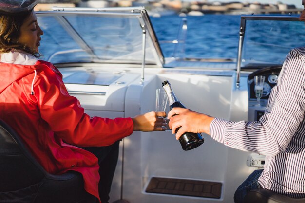 schöne junge Frau in einem roten Mantel Champagner auf einer Yacht trinken.