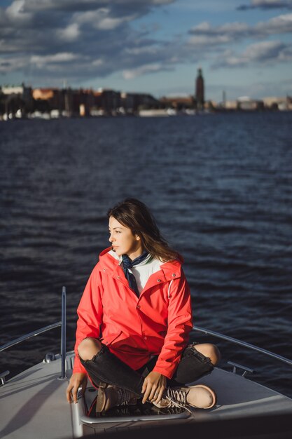 schöne junge Frau in einem roten Regenmantel reitet eine private Yacht. Stockholm, Schweden