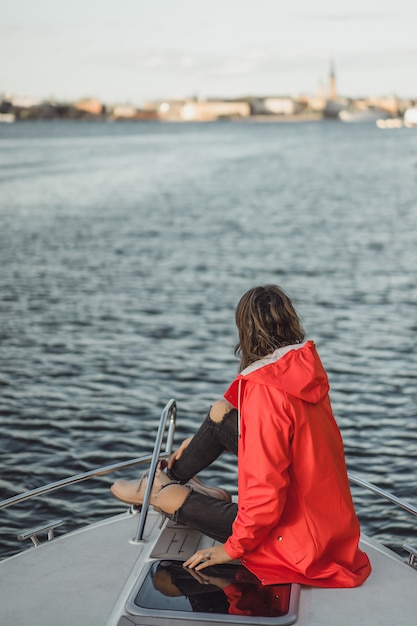 schöne junge Frau in einem roten Regenmantel reitet eine private Yacht. Stockholm, Schweden