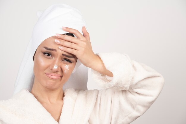 Schöne junge Frau in einem weißen Bademantel, der auf einer weißen Wand aufwirft.