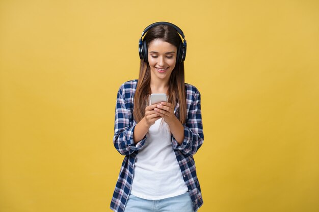 Schöne junge Frau in Kopfhörern, die Musik hören und auf gelbem Hintergrund singen.