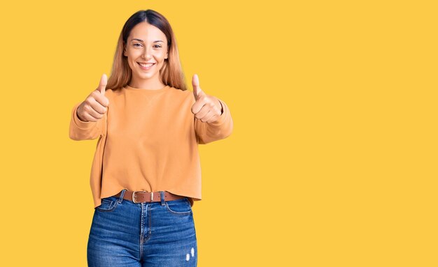 Schöne junge Frau in lässiger Kleidung, die positive Gesten mit der Hand, Daumen nach oben, lächelnd und glücklich über den Erfolg genehmigt. Siegergeste.